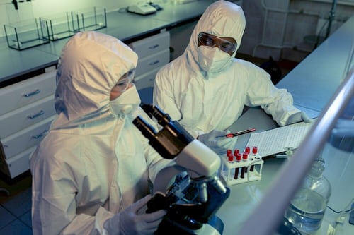 Two scientists in lab coats and masks examining samples in a laboratory, related to cancer research or drug development.