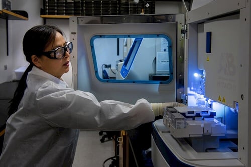 A female scientist working with a laboratory machine, related to genetic research.