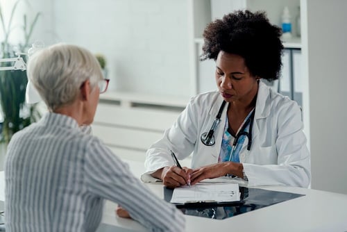 A female doctor filling out consent forms at a desk, with the patient seated across from her on the other side.