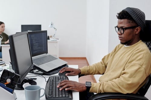 A person working at a desk with two screens, coding on one, symbolizing the secure and technology-driven environment of clinical trial data management.