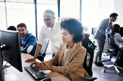A group of people working at their desks, with two women collaborating on screens, illustrating a positive and engaged workforce at Viedoc.