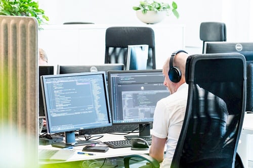 A Viedoc team member working at his desk with two screens, coding and contributing to the development of secure technologies and resources for clinical trials.