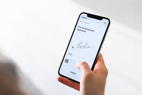 A smartphone displaying a screenshot of the Viedoc Me interface with an e-signature feature visible.