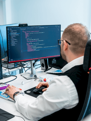Majd Mirza, a Viedoc employee, sitting in front of computers displaying coding on their screens, representing a focus on data privacy, security, and compliance.