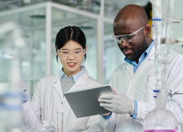 Mobile-Man in lab coat looking at tablet with woman in lab coat holding flask