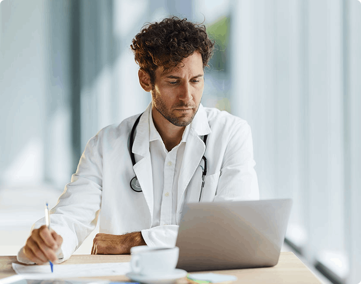 man in labcoat looking at laptop screen and holding pen